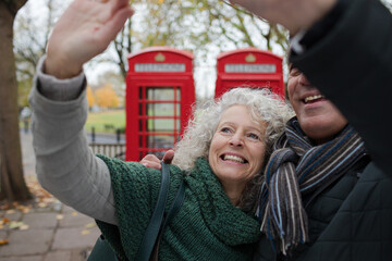 Smiling senior couple taking selfie in autumn park in front of red telephone booths