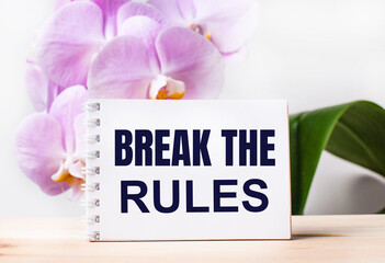 White blank notebook with the text BREAK THE RULES on the table against the background of a light pink orchid.
