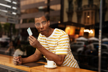 Handsome young african man in cafe drinking coffee. Portrait of happy man with credit card drinking coffee in cafe.