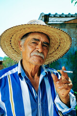 Fototapeta premium Senior man wearing hat while holding cigarette at farm on sunny day