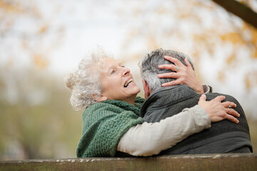Smiling, affectionate senior couple hugging on bench in autumn park
