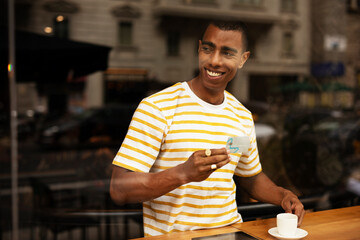 Handsome young african man in cafe drinking coffee. Portrait of happy man with credit card drinking coffee in cafe.