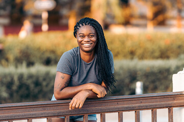 Afro woman leaning on a rail while smiling to the camera outdoors