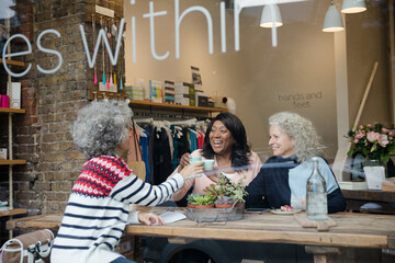 Laughing active senior women friends eating dessert at  cafe