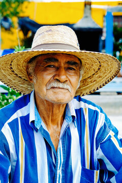 Portrait of senior man with mustache wearing hat and striped shirt sitting at farm