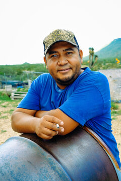 Portrait of smiling man wearing cap standing leaning on metal barrel while smoking cigarette at farm