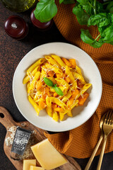 Neapolitan pasta penne rigate with pumpkin in a ceramic plate on a dark culinary background top view. Traditional Italian cuisine