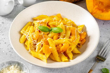 Neapolitan pasta penne rigate with pumpkin in a ceramic plate on a light gray culinary background close-up. Traditional Italian cuisine
