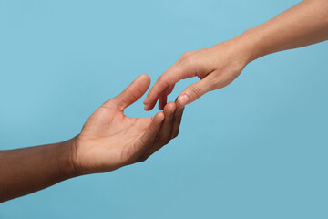 Woman and African American man touching hands on light blue background, closeup