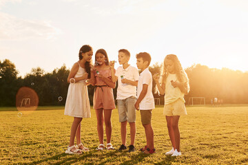 Illuminated by sunlight. Standing on the sportive field. Group of happy kids is outdoors at daytime