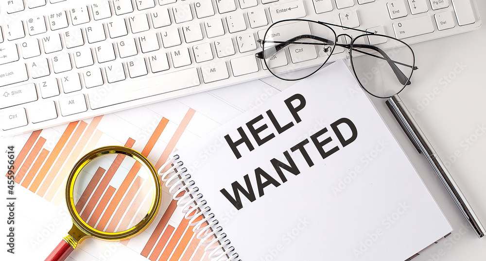 Aufkleber help wanted text written on notebook with keyboard, chart,and glasses