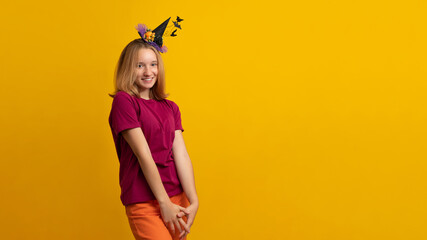 Banner. Happy Halloween witch with a black hat. Beautiful young smiling woman in witches hat and costume on yellow background.