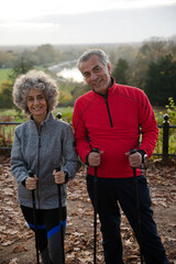 Smiling, affectionate senior couple with walking sticks in park