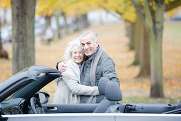 Affectionate, tender senior couple hugging in autumn park near car