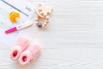 Pregnancy test with pink baby girl booties and calendar, top view