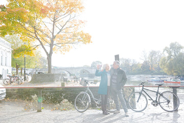 Obraz premium Senior couple with bicycles taking selfie at autumn river