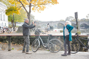 Obraz premium Senior man photographing wife with bicycle in autumn city