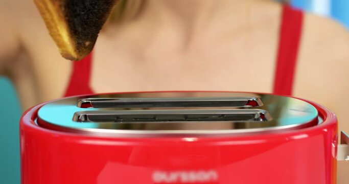 The girl takes out burnt bread from the toaster. 