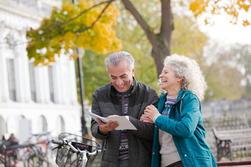 Senior couple with bicycles traveling, looking at guidebook along autumn river