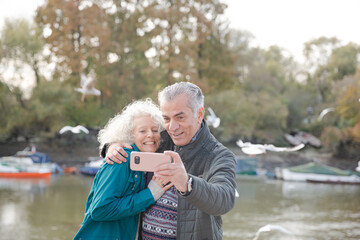Playful senior couple taking selfie at pond in park