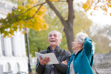 Senior couple with bicycles traveling, looking at guidebook along autumn river