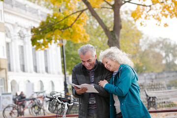 Senior couple with bicycles traveling, looking at guidebook along autumn river
