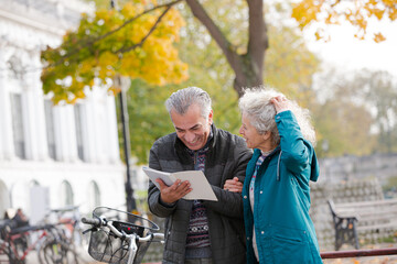 Senior couple with bicycles traveling, looking at guidebook along autumn river