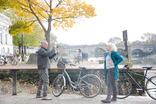 Senior man photographing wife with bicycle in autumn city