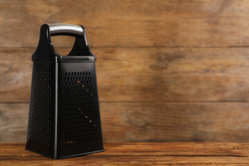 Modern black grater on wooden table. Space for text