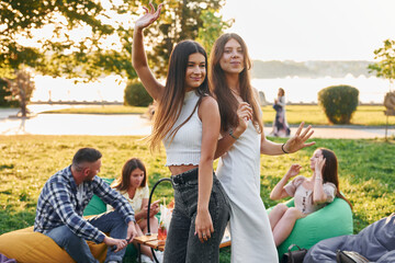 Women posing for the camera. Group of young people have a party in the park at summer daytime