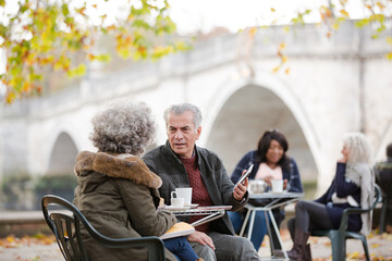 Obraz na płótnie Canvas Senior couple using digital tablet, enjoying coffee and tea at autumn park