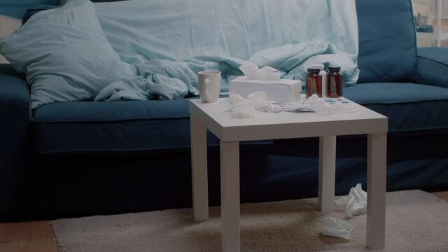 Nobody in living room with medicaments and cup of tea on table. Empty space with couch and bottles of pills, tablets of capsules, thermometer and tissues for person with sickness.