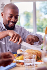 Father Carving As Multi Generation Family Sit Around Table At Home And Enjoy Eating Meal Together