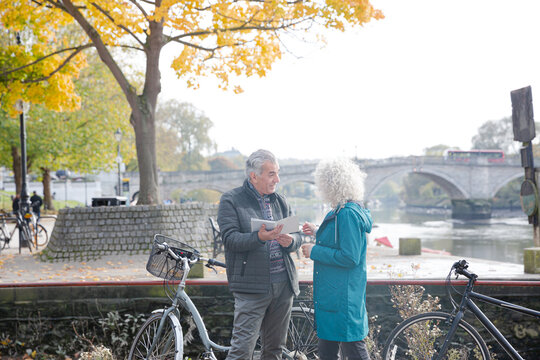 Senior couple with bicycles traveling, looking at guidebook along autumn river - Powered by Adobe
