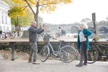 Obraz premium Senior man photographing wife with bicycle in autumn city