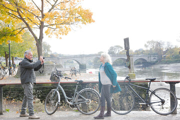 Obraz premium Senior man photographing wife with bicycle in autumn city