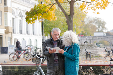 Senior couple with bicycles traveling, looking at guidebook along autumn river