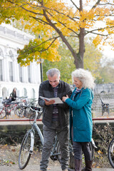 Senior couple with bicycles traveling, looking at guidebook along autumn river