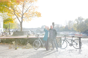 Senior couple with bicycles taking selfie at autumn river