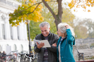 Senior couple with bicycles traveling, looking at guidebook along autumn river