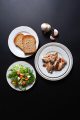 top view of table set with chicken dishes, salad, wholemeal bread, water and garlic. Black background with copy space.