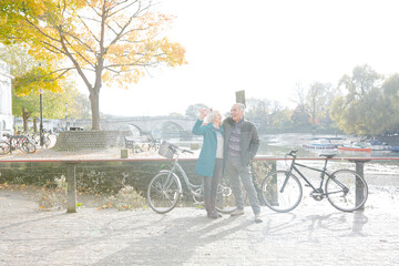 Obraz premium Senior couple with bicycles taking selfie at autumn river