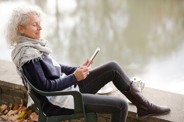Active senior woman using digital tablet at park pond
