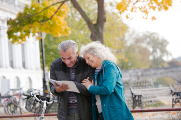 Senior couple with bicycles traveling, looking at guidebook along autumn river