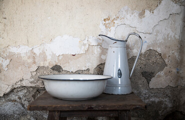 Old water basin and pitcher on wooden table against wall