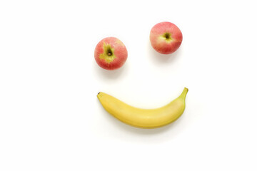 Cheerful face made from fresh ripe fruits isolated on white background, big eyes one above the other from red apples, smile from yellow banana, anthropomorphic face happy, flat lay, copy space.