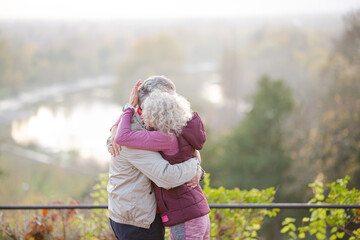 Affectionate active senior couple hugging at park pond