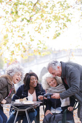 Active senior friends using digital camera at autumn sidewalk cafe