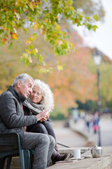 Active senior couple talking, enjoying coffee at autumn park cafe