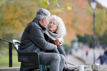 Active senior couple talking, enjoying coffee at autumn park cafe